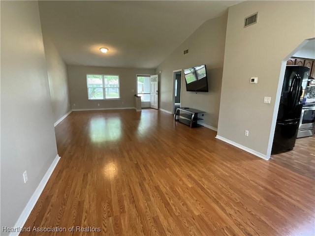 unfurnished living room featuring wood finished floors, baseboards, high vaulted ceiling, and arched walkways