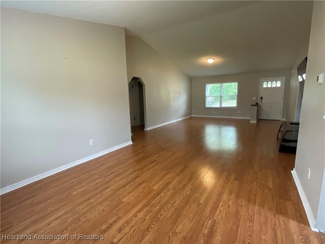 unfurnished living room with baseboards, wood finished floors, and vaulted ceiling