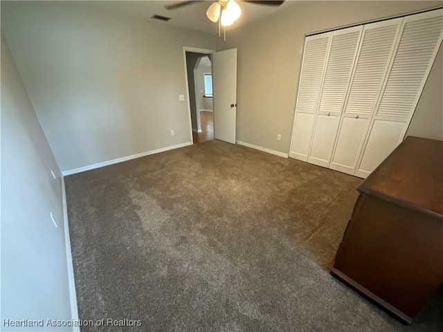 unfurnished bedroom featuring dark carpet, baseboards, a closet, and a ceiling fan