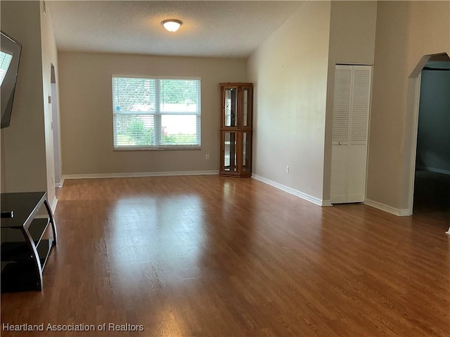 unfurnished living room with arched walkways, wood finished floors, and baseboards