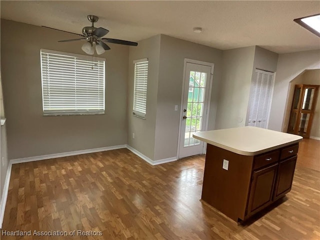 kitchen featuring light wood-style flooring, light countertops, baseboards, ceiling fan, and a center island