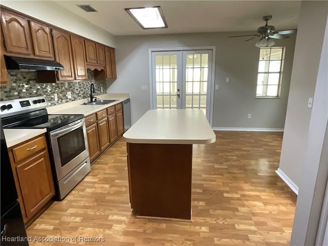 kitchen with stainless steel range with electric stovetop, a sink, under cabinet range hood, light wood-style floors, and a center island