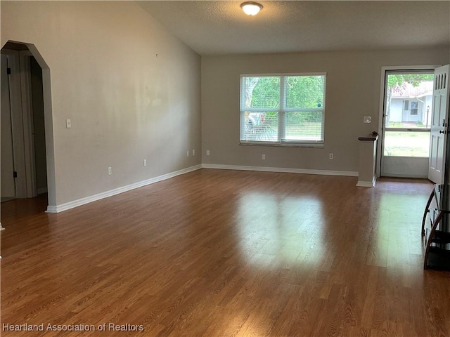 unfurnished living room featuring arched walkways, healthy amount of natural light, wood finished floors, and baseboards