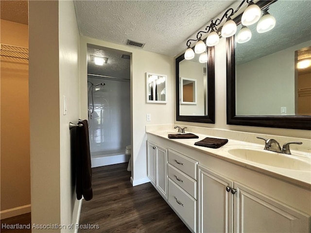 bathroom featuring toilet, wood finished floors, a sink, visible vents, and walk in shower