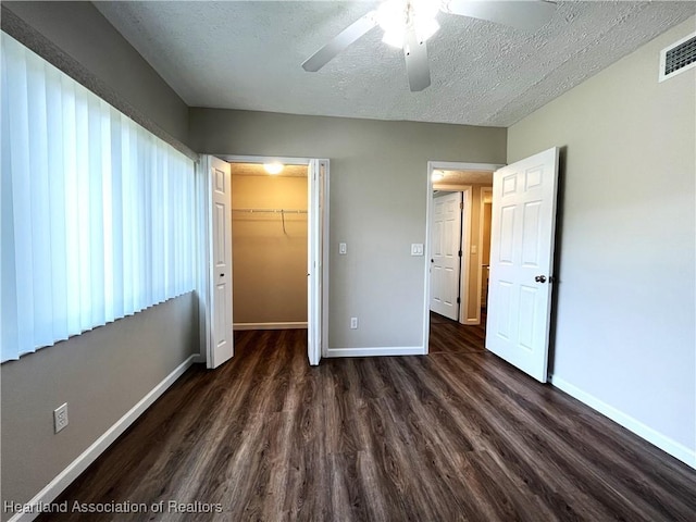 unfurnished bedroom with a textured ceiling, visible vents, baseboards, a spacious closet, and dark wood finished floors