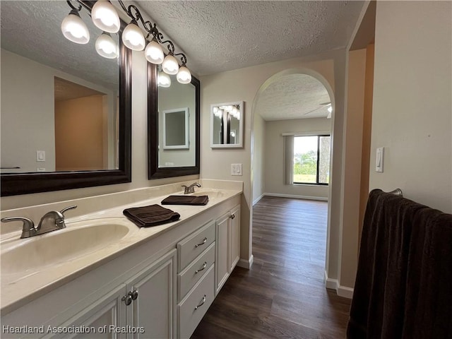 full bath with double vanity, a textured ceiling, a sink, and wood finished floors