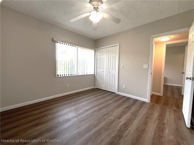 unfurnished bedroom with baseboards, dark wood-style floors, ceiling fan, a textured ceiling, and a closet