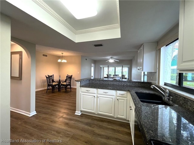 kitchen featuring dark wood finished floors, a raised ceiling, white cabinets, a sink, and a peninsula