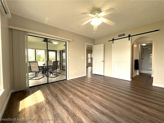 unfurnished room featuring a barn door, arched walkways, visible vents, ceiling fan, and dark wood-type flooring