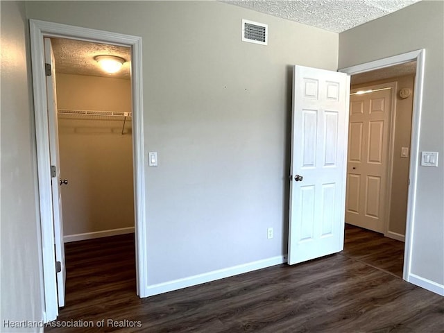 unfurnished bedroom featuring baseboards, visible vents, dark wood-style flooring, and a textured ceiling