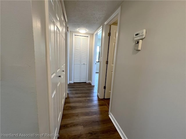 corridor featuring dark wood-style flooring, a textured ceiling, and baseboards