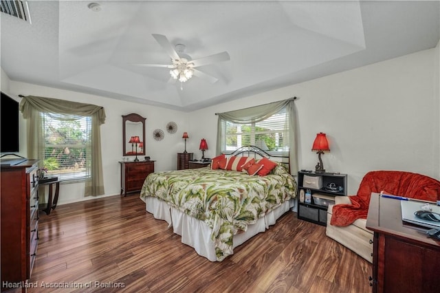 bedroom featuring dark wood-style floors, a raised ceiling, visible vents, and a ceiling fan