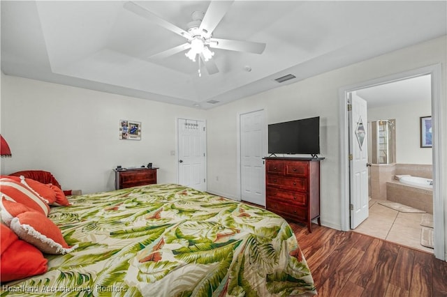 bedroom featuring visible vents, ensuite bath, ceiling fan, wood finished floors, and a tray ceiling