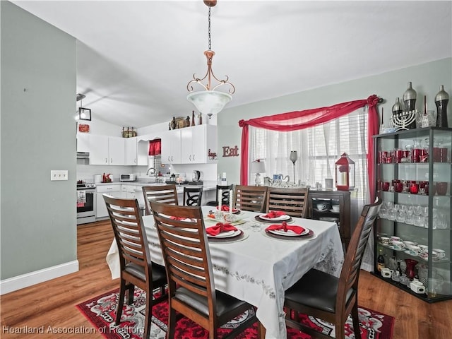 dining area with light hardwood / wood-style floors, lofted ceiling, and sink