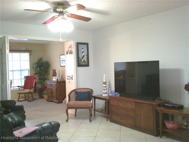 living area featuring light tile patterned flooring, ceiling fan, and a textured ceiling