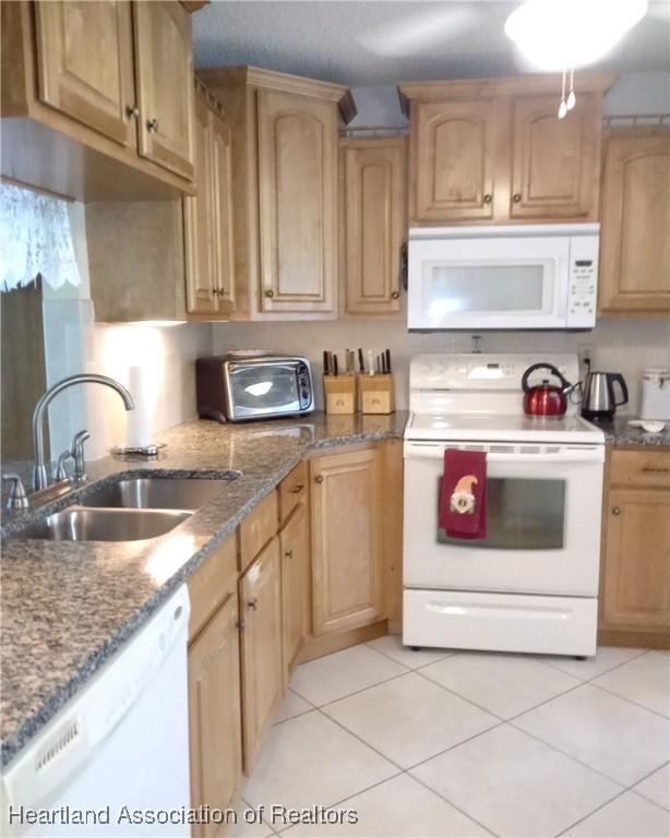 kitchen featuring a toaster, white appliances, a sink, stone countertops, and light tile patterned floors
