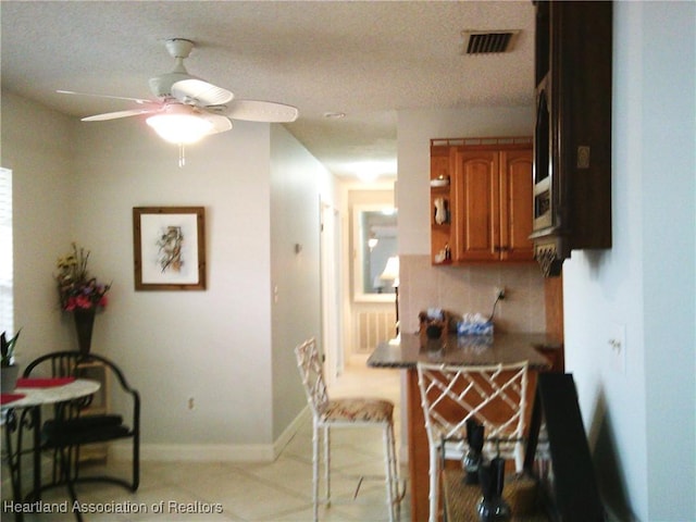 kitchen featuring baseboards, decorative backsplash, visible vents, a ceiling fan, and brown cabinets