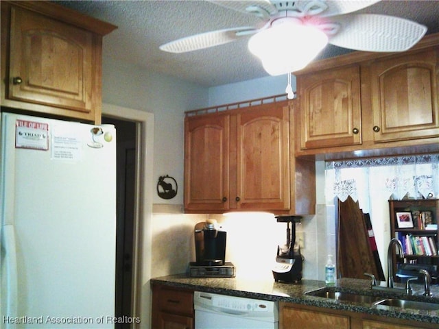 kitchen with a sink, dark stone countertops, brown cabinetry, and white appliances