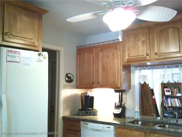 kitchen featuring a ceiling fan, a sink, dark stone countertops, refrigerator, and white dishwasher