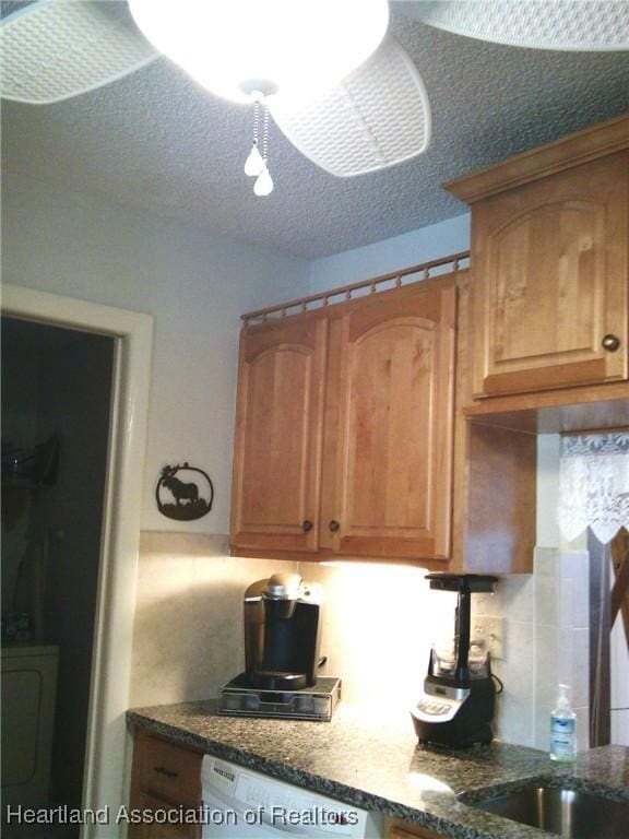 kitchen with brown cabinets, tasteful backsplash, a textured ceiling, dark stone counters, and dishwasher