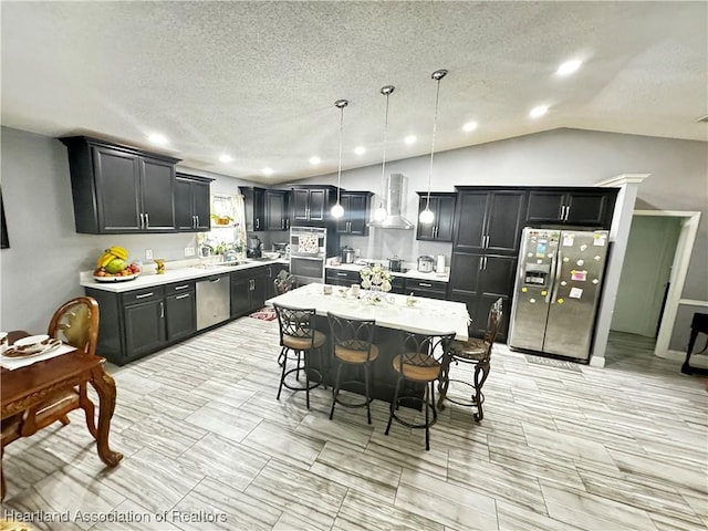 kitchen featuring a center island, wall chimney range hood, lofted ceiling, decorative light fixtures, and appliances with stainless steel finishes