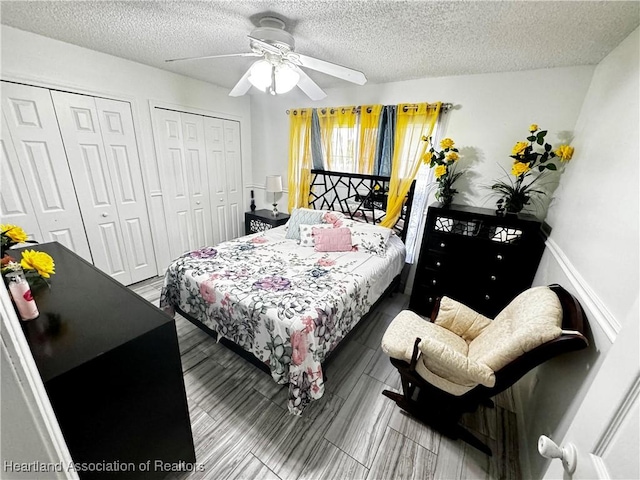 bedroom with ceiling fan, a textured ceiling, and two closets