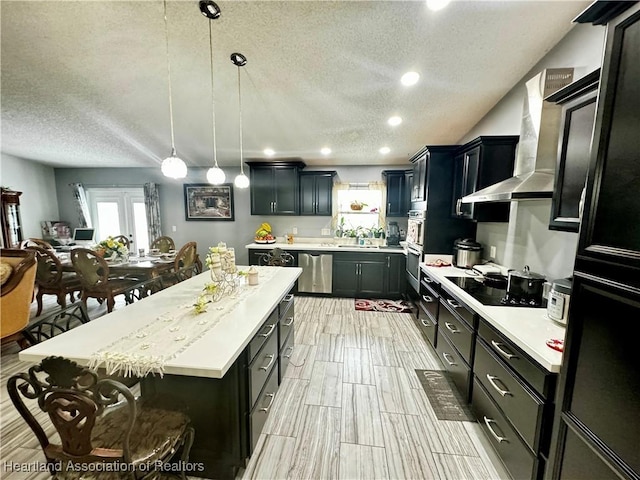 kitchen with wall chimney exhaust hood, hanging light fixtures, stainless steel dishwasher, black electric cooktop, and a kitchen island