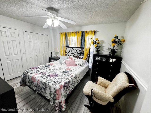 bedroom with two closets, ceiling fan, light hardwood / wood-style floors, and a textured ceiling