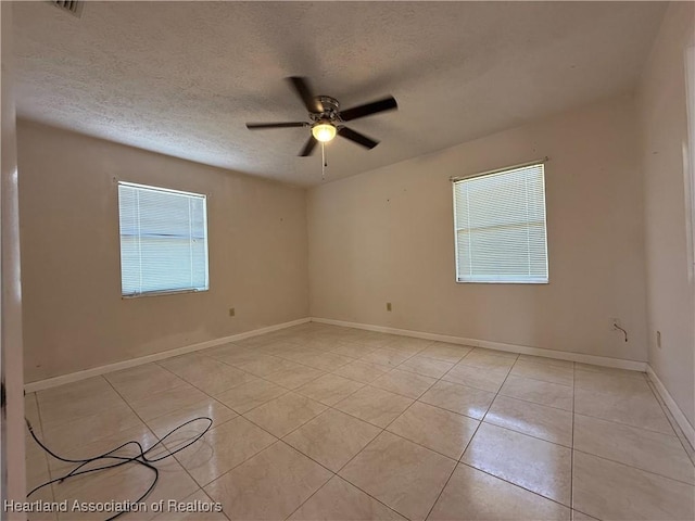 empty room featuring light tile patterned floors, baseboards, a textured ceiling, and ceiling fan