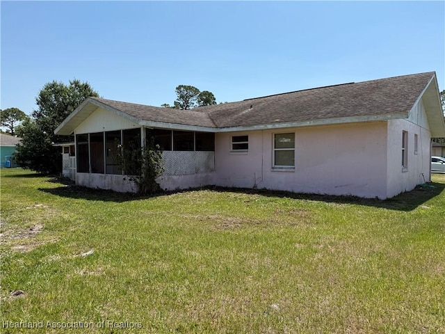 back of house with a lawn, a sunroom, a shingled roof, and stucco siding