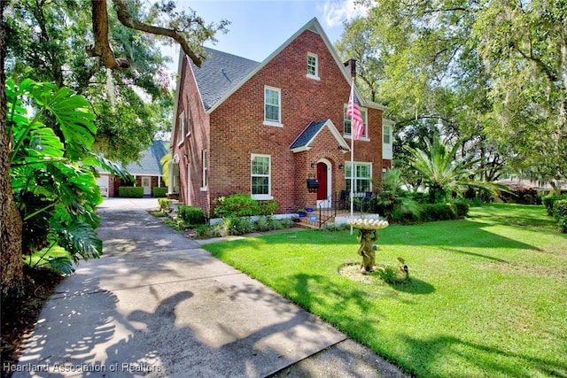 1237 Hotiyee Ave, Sebring, FL 33870 - tudor-style house with brick siding, a front yard, a shingled roof, a garage, and a chimney