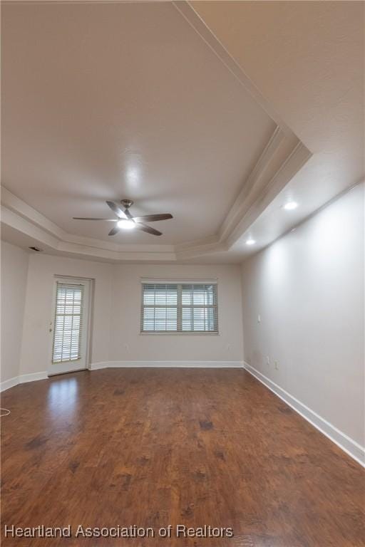 unfurnished room with a raised ceiling, ceiling fan, and dark hardwood / wood-style floors