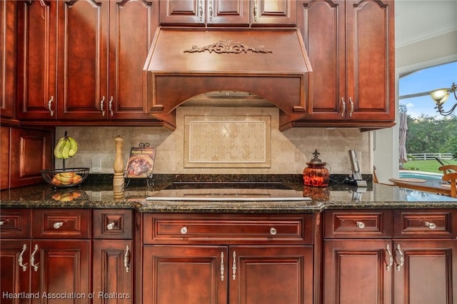 kitchen with tasteful backsplash, stovetop, dark stone counters, and premium range hood