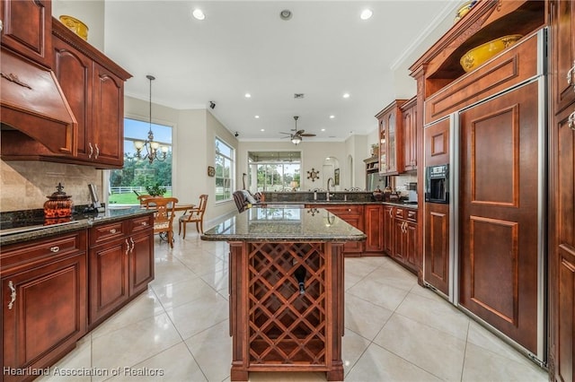 kitchen with kitchen peninsula, dark stone counters, pendant lighting, ceiling fan with notable chandelier, and ornamental molding