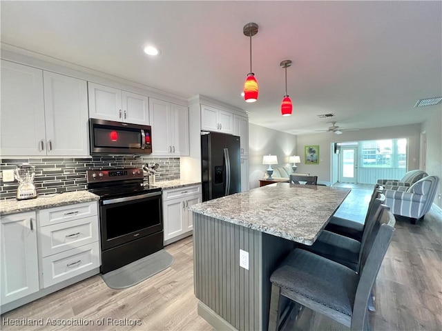 kitchen with a breakfast bar, white cabinetry, hanging light fixtures, stainless steel appliances, and light stone counters