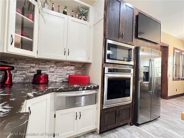 kitchen with light hardwood / wood-style flooring, dark stone countertops, tasteful backsplash, white cabinetry, and stainless steel appliances