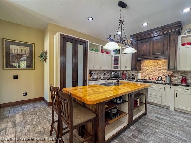 kitchen featuring sink, wood counters, wood-type flooring, decorative light fixtures, and white cabinets