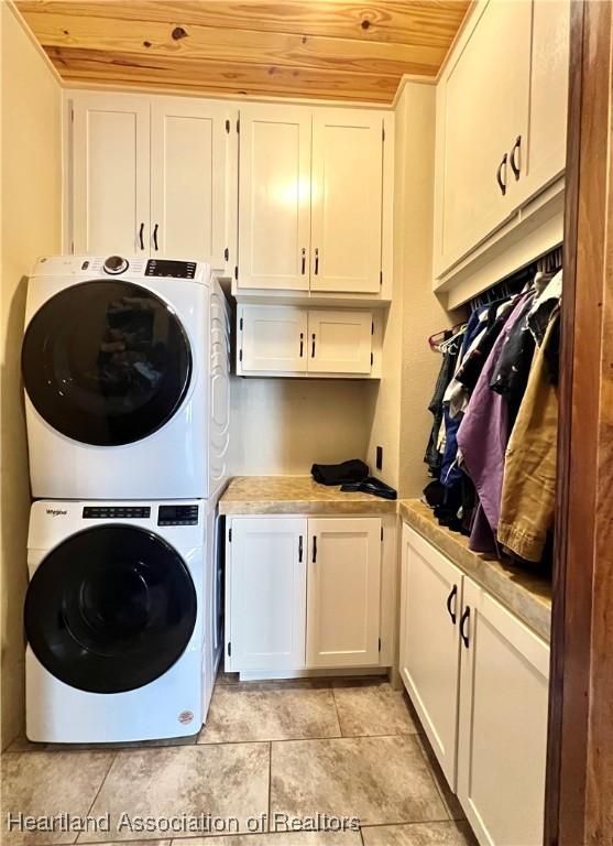 laundry area featuring cabinets, wooden ceiling, and stacked washer and clothes dryer