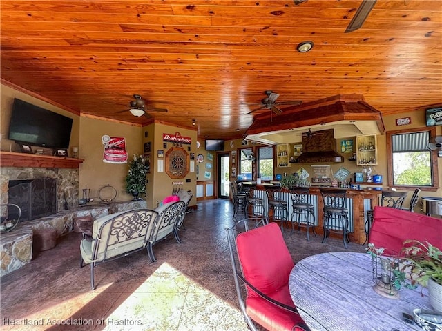 dining space with a stone fireplace, ceiling fan, and wooden ceiling