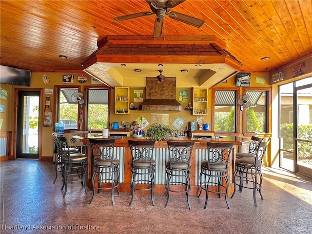 interior space with a breakfast bar, premium range hood, ceiling fan, and wooden ceiling