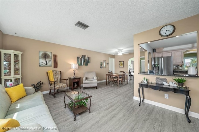 living room with ceiling fan, a textured ceiling, and light hardwood / wood-style flooring