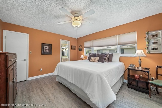 bedroom with a textured ceiling, ensuite bath, light hardwood / wood-style flooring, and ceiling fan