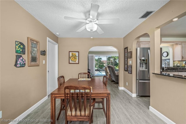 dining room featuring ceiling fan, sink, light hardwood / wood-style floors, and a textured ceiling