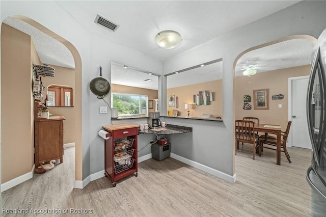 interior space featuring stainless steel refrigerator, ceiling fan, light hardwood / wood-style flooring, and a textured ceiling