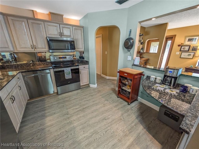 kitchen featuring a textured ceiling, kitchen peninsula, stainless steel appliances, and light hardwood / wood-style flooring