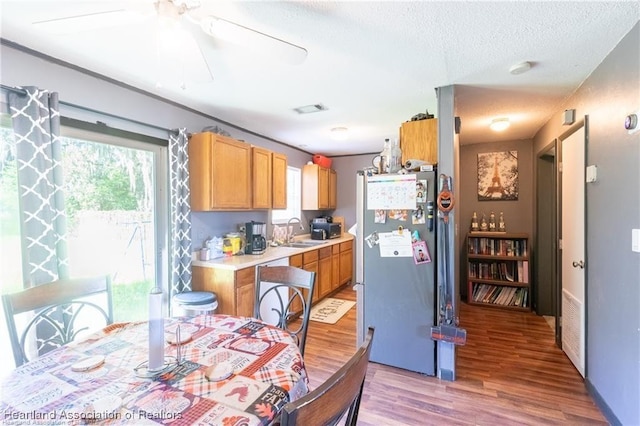 kitchen featuring sink, light hardwood / wood-style flooring, a textured ceiling, stainless steel refrigerator, and ceiling fan