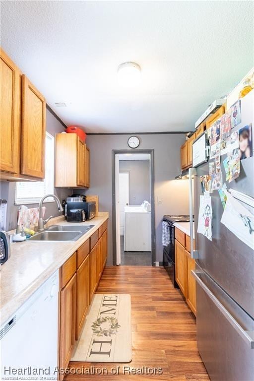 kitchen with black electric range oven, sink, stainless steel refrigerator, white dishwasher, and washer / clothes dryer