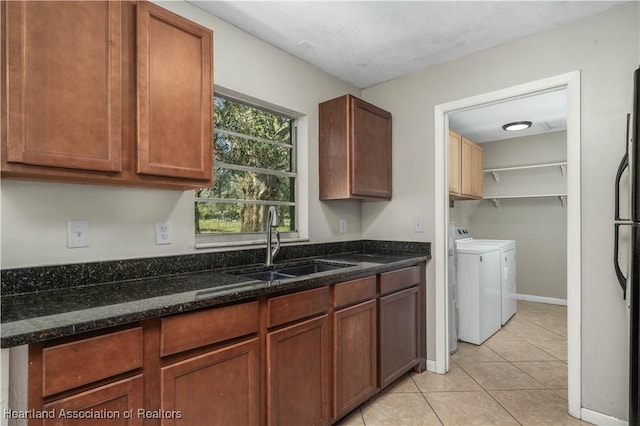 kitchen with washing machine and clothes dryer, dark stone countertops, sink, and light tile patterned floors