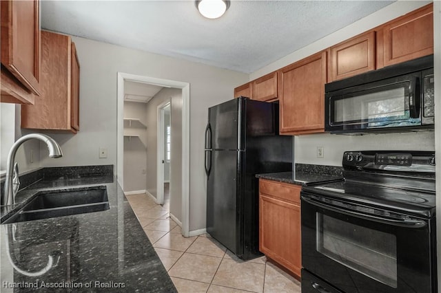 kitchen with dark stone countertops, sink, light tile patterned floors, and black appliances