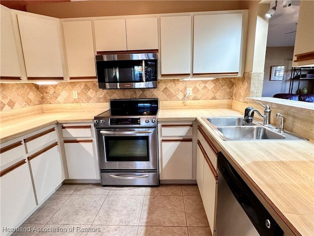 kitchen with a sink, white cabinetry, stainless steel appliances, light tile patterned floors, and decorative backsplash